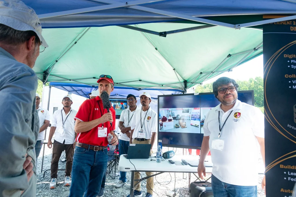 Presenters beside a video display at the collaborative remote robotics experiment at ArtIAMAS 2024