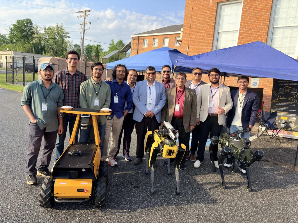 A group posing with wheeled and quadruped robots outside the CYPRESS Technology Research Center