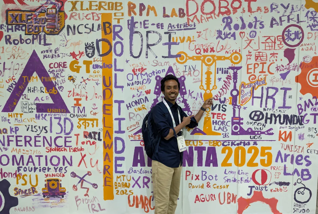 A conference attendee standing in front of the colorful ICRA 2025 mural